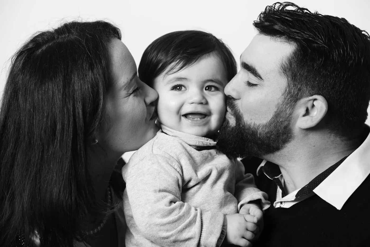 Parents embrassant sur les joues leur bébé souriant, portrait de famille en noir et blanc