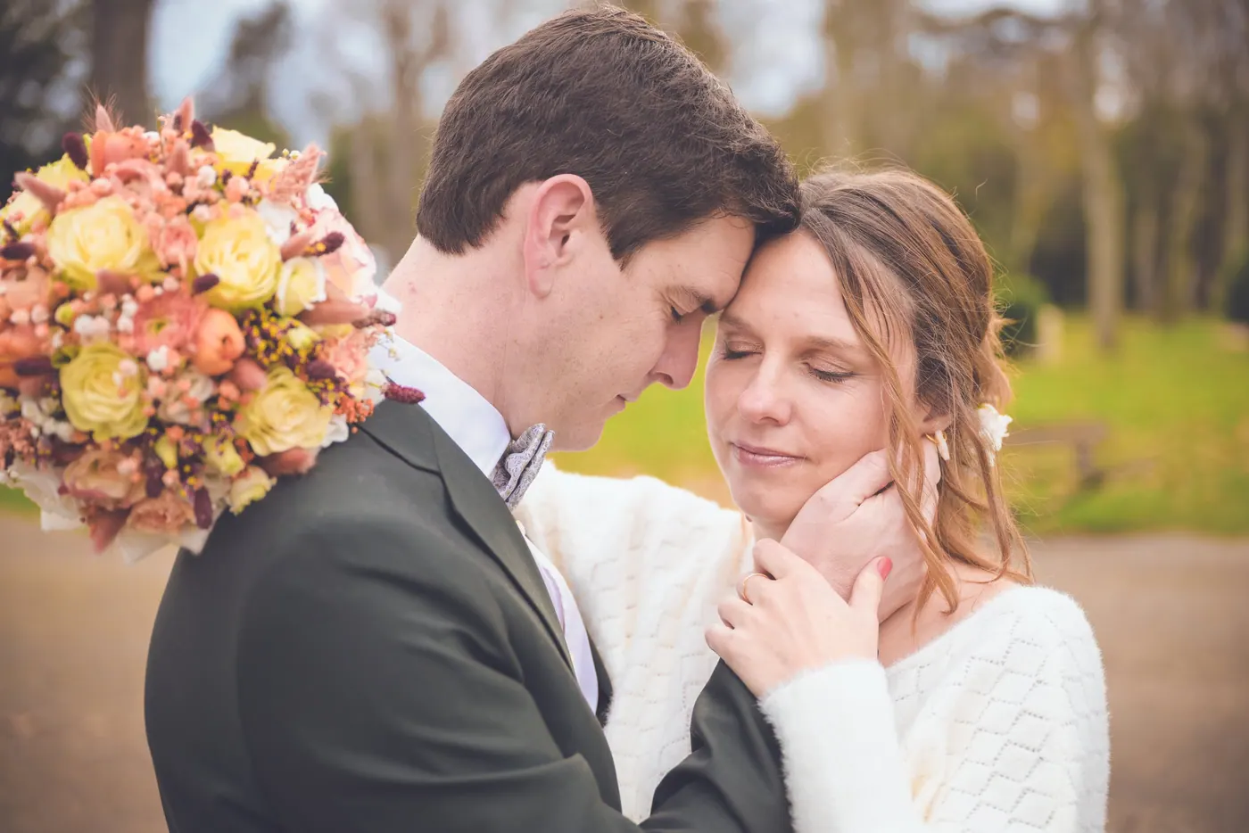 Les mariés front contre front, la mariée les yeux fermés, le bouquet d'automne au premier plan